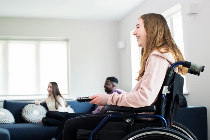 Laughing girl in wheelchair holding a television remote, watching television with friends