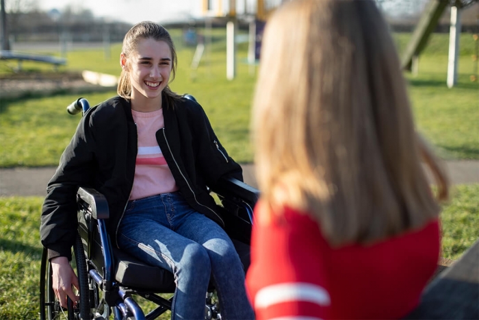 Smiling girl in wheelchair in playground talking with a friend