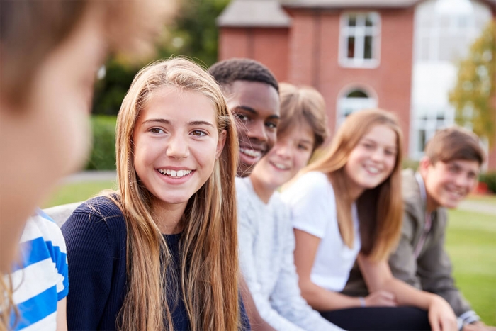 Smiling group of teenage students sitting outside of a school