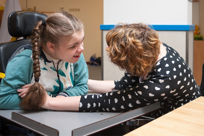 A young girl with learning disabilities talking to an adult helping her