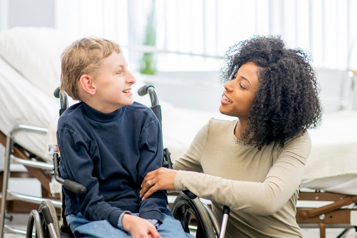 A young adult helping and smiling with a young person in a wheelchair