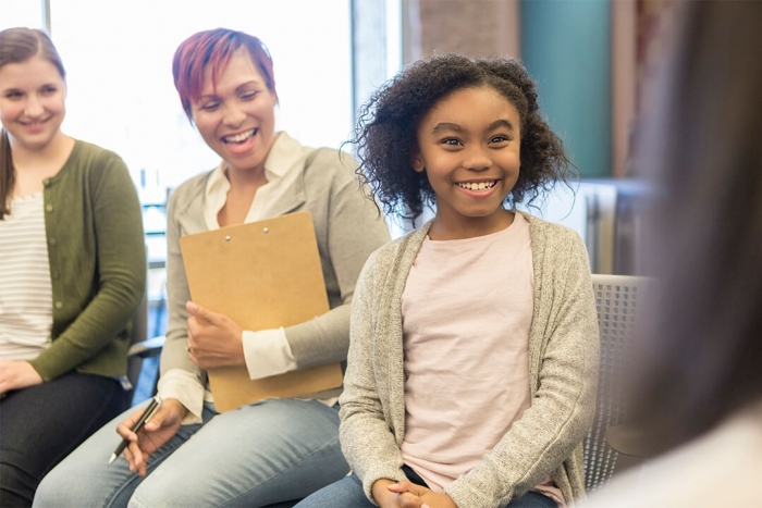 A smiling young girl sitting with 2 adults