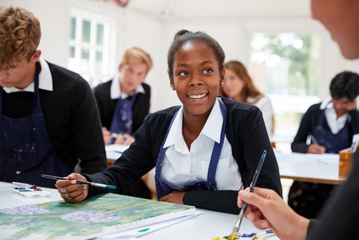 Smiling girl in secondary school painting with a group of students